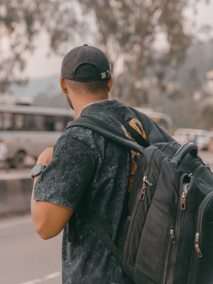 Traveler wearing backpack and baseball cap standing on road, outdoors.
