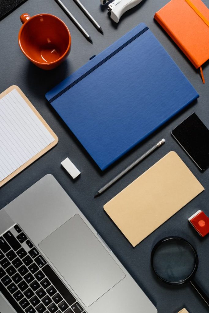 Flat lay of office essentials including a laptop, notebooks, and gadgets for a modern workspace.