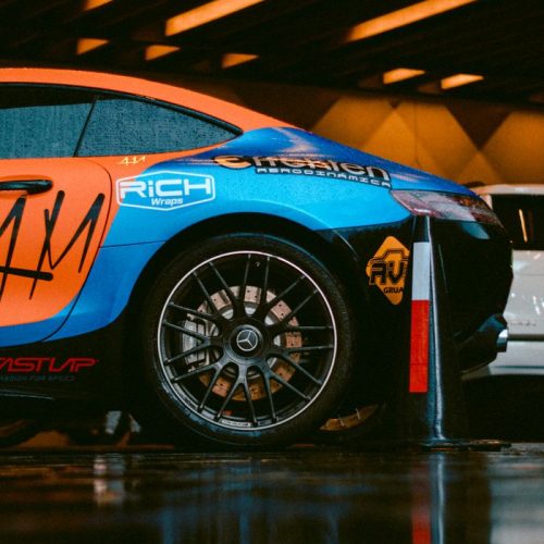 Vividly wrapped sportscar showcased indoors with a wet floor reflection.