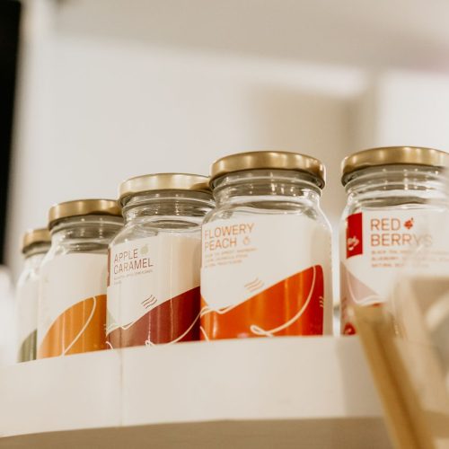 Glass jars with various labels on a shelf display in a store setting.