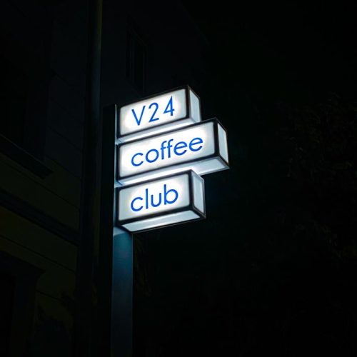 An illuminated sign for a coffee club at night with a dark background.