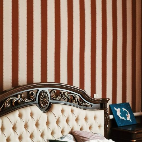Luxurious bedroom featuring a carved wooden headboard and striped wallpaper for a classic look.