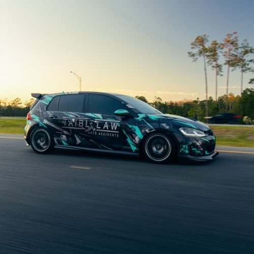 A sleek sports car with custom graphics speeds down a highway at sunset, showcasing its design.