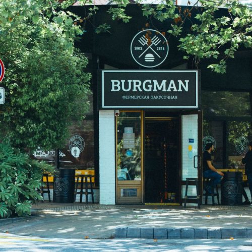 Exterior view of Burgman restaurant with outdoor seating area in a leafy urban setting.