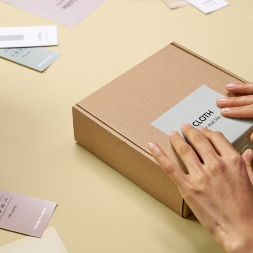 Hands carefully packing a cardboard box with multiple tags around, emphasizing sustainable packaging.